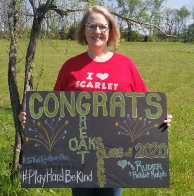 Eryn Ruder wears a red shirt that reads "I heart Scarlet". She is holding a black sign that reads Congrats Great Oaks Scarlet class of 2020"