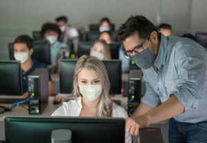 Teacher wearing a facemask and helping female student at an IT class - education during the COVID-19 pandemic